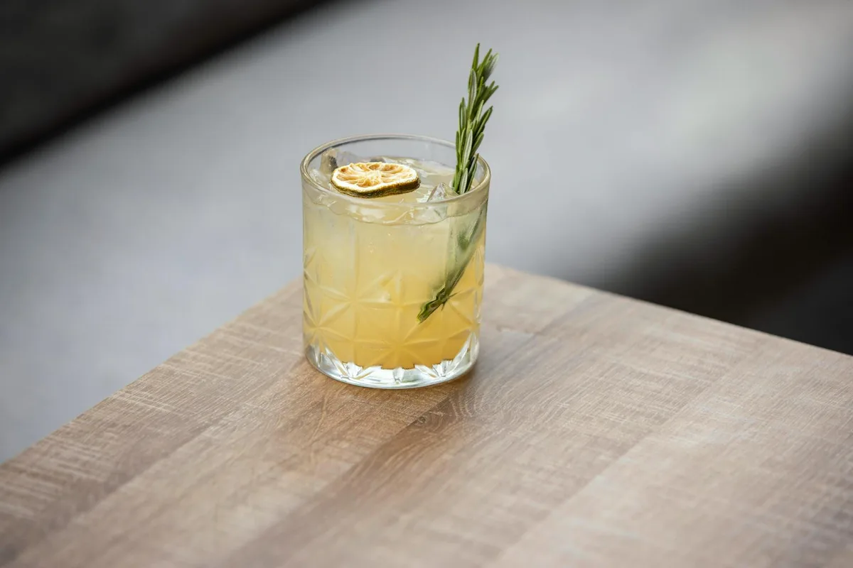 Zitrus-Cocktail garniert mit getrockneter Zitronenscheibe und Rosmarin auf einem Holztisch