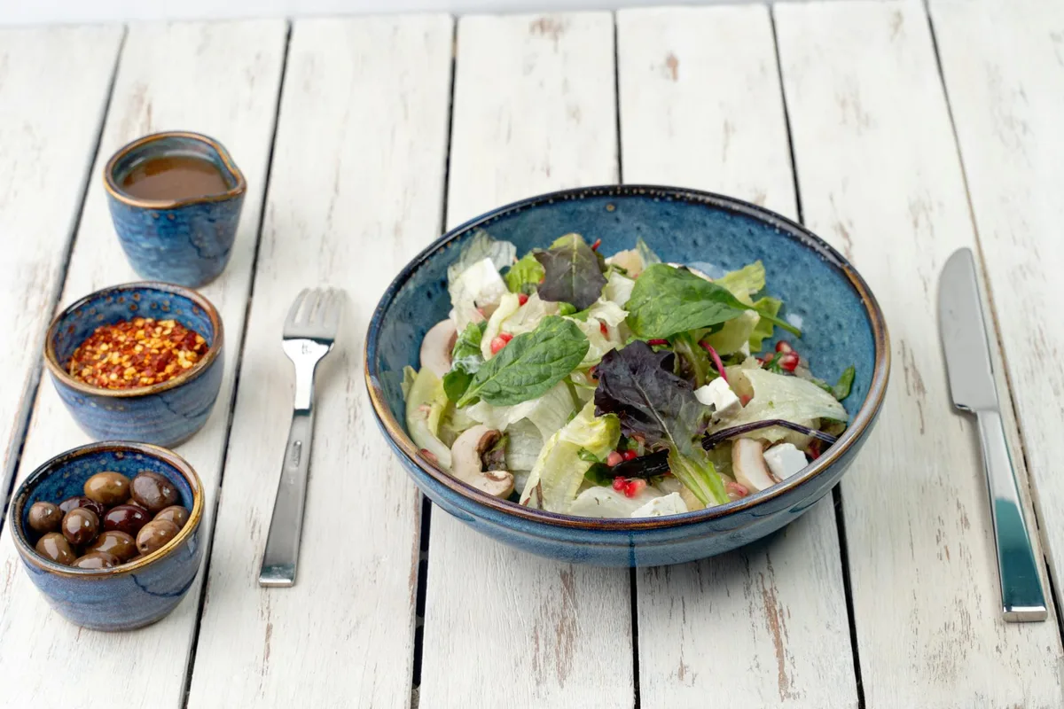 Insalata mediterranea fresca con olive, feta e verdure verdi su tavolo bianco rustico