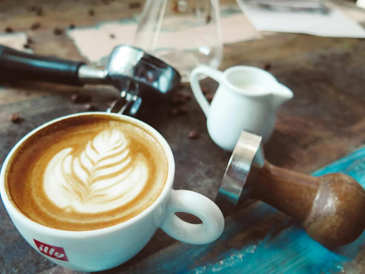 Latte com arte elegante em mesa rústica com jarra de leite e tamper