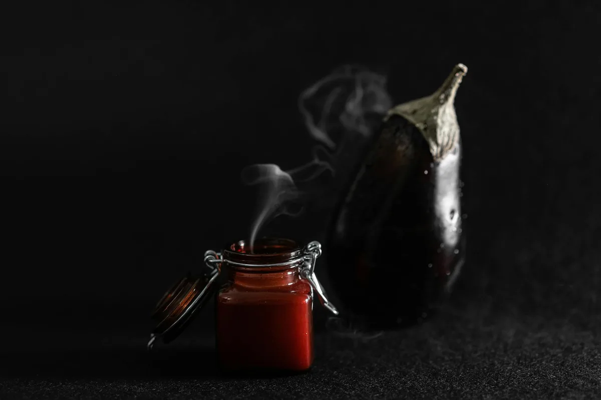 Composizione minimalista con melanzana e barattolo fumante su sfondo scuro