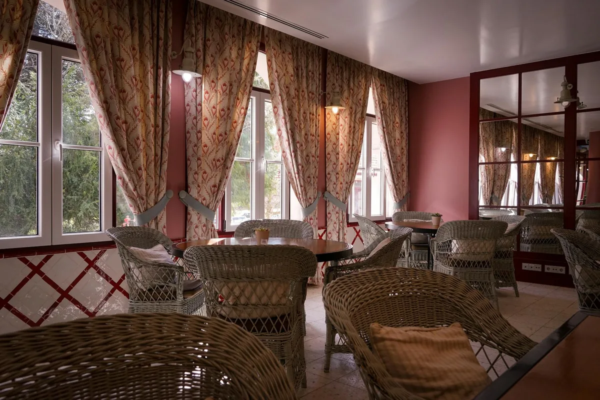 Gemütliches Café-Interieur mit Korbstühlen, runden Tischen und dekorativen Vorhängen bei natürlichem Lichteinfall