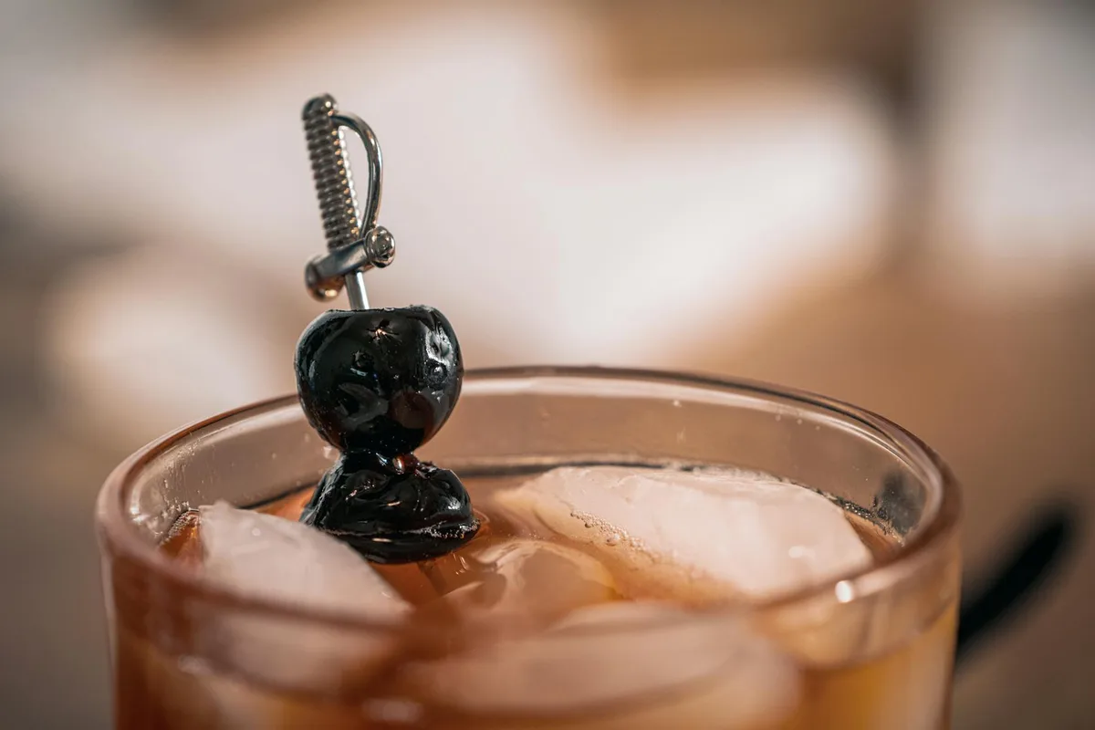 Erfrischender Cocktail mit Eiswürfeln und dekorativem Schwert-Rührstab in einem Glas