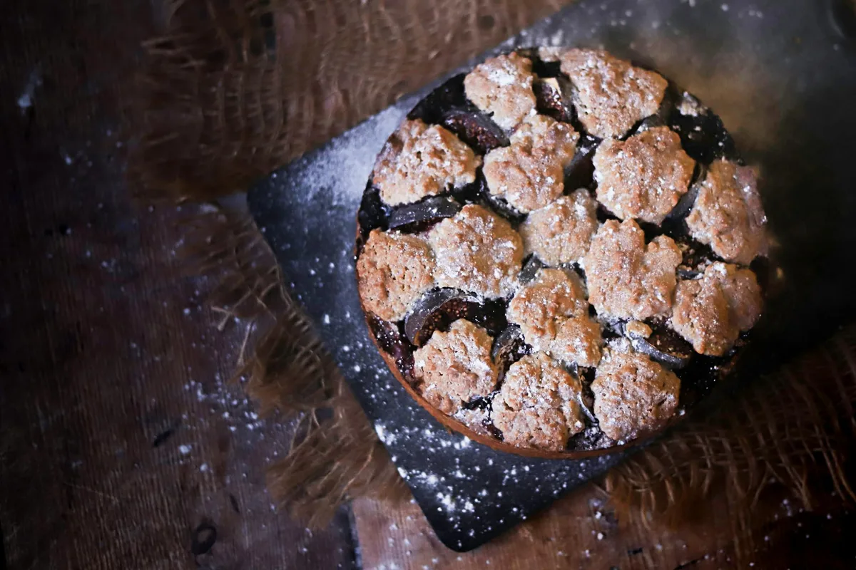 Rustikaler Feigenkuchen mit Streusel und Puderzucker auf einem Holztisch