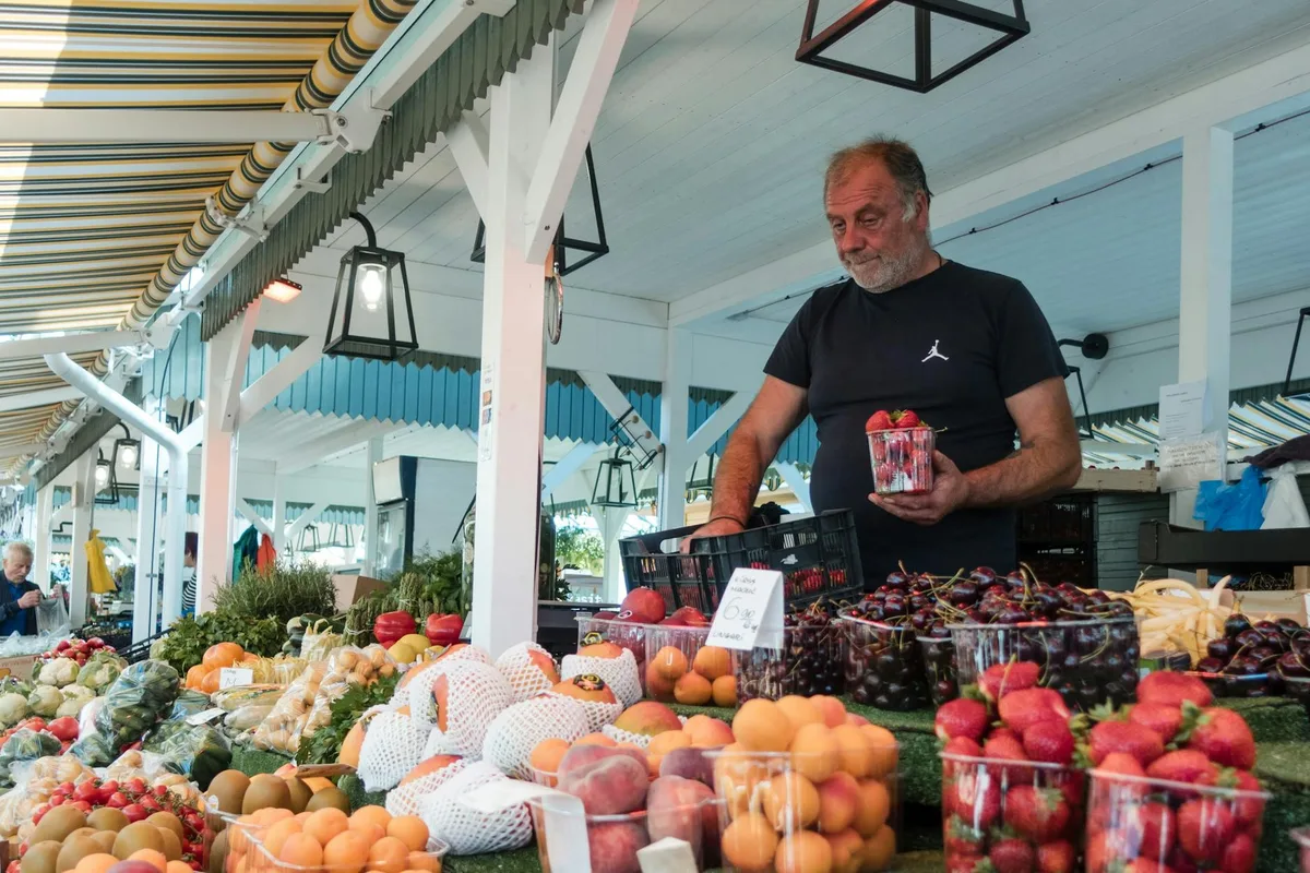 A vendor selling a variety of fresh fruits at a vibrant market stall under a striped canopy.