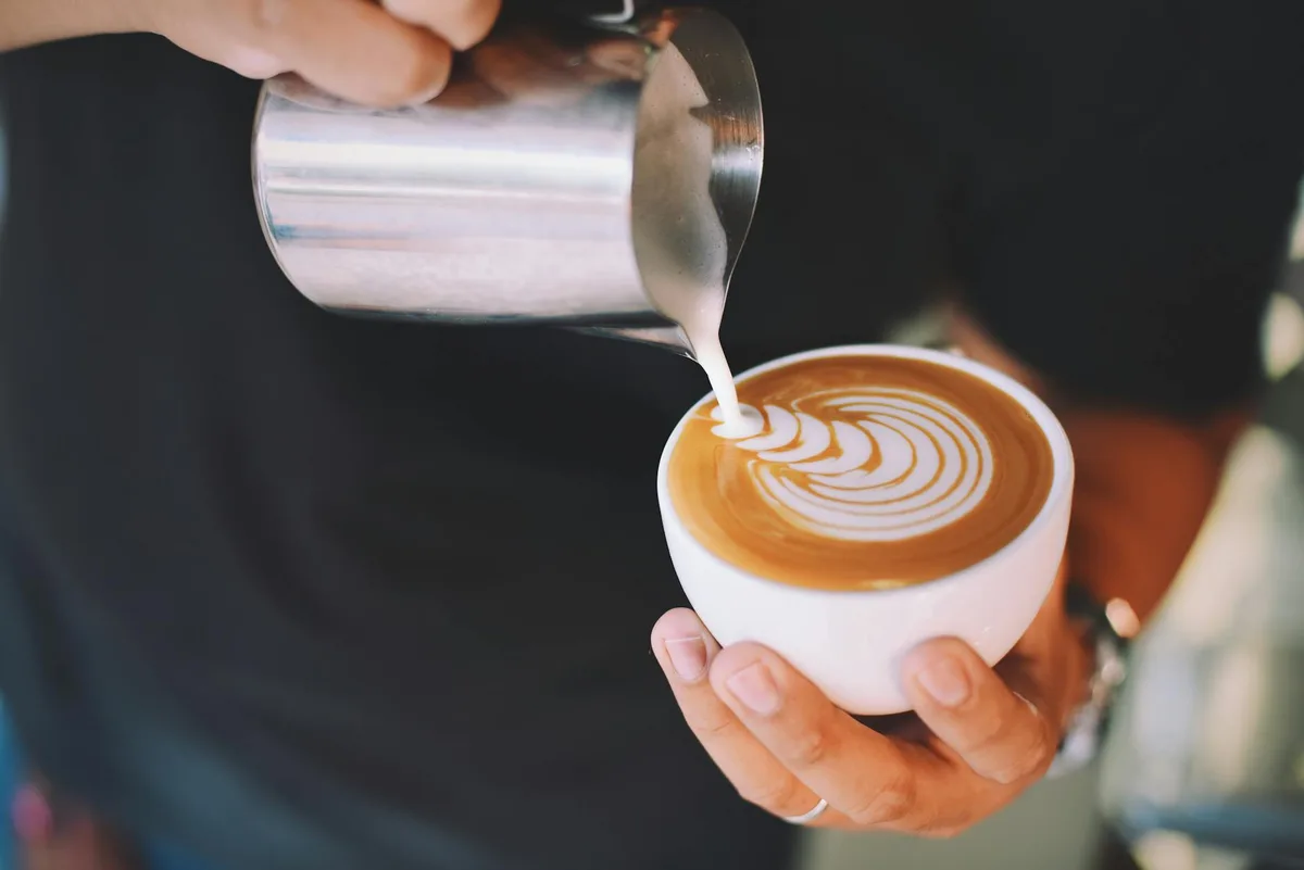 Barista despejando arte em leite em cappuccino, demonstrando latte art