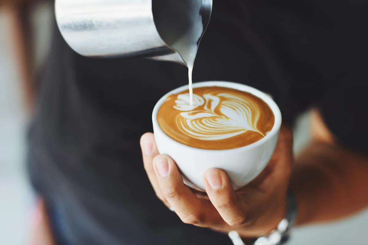 Barista versant du lait pour créer un latte art dans une tasse de café