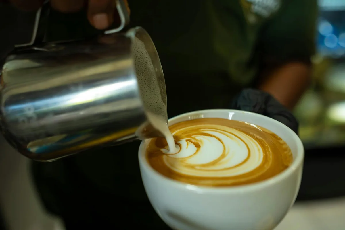 Крупный план баристы, наливающего молоко для создания латте-арт в чашке кофе