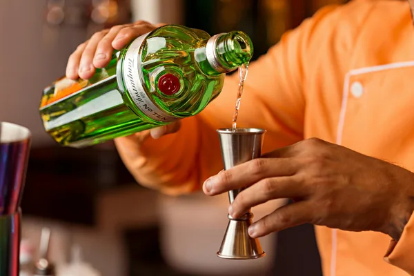 Nahaufnahme eines Barkeepers, der Gin in einen Jigger für die Cocktailzubereitung gießt