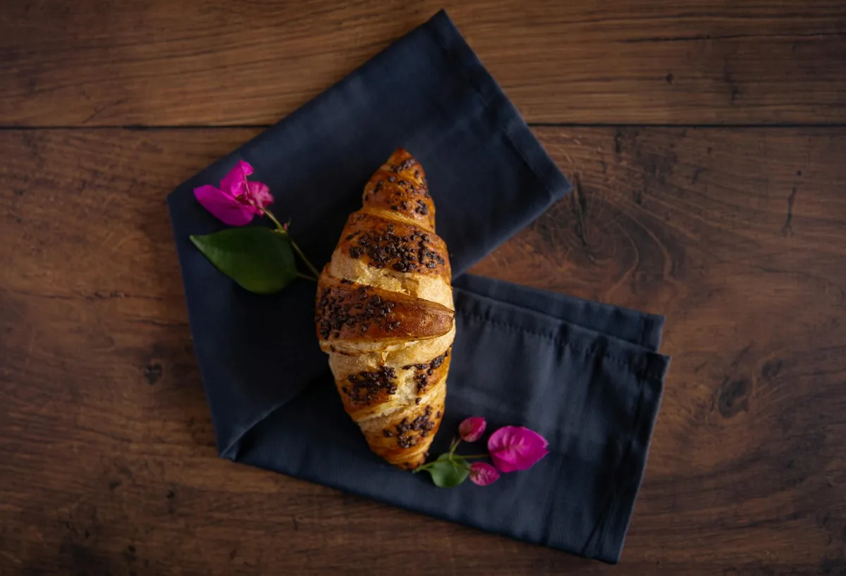 Nahaufnahme eines Croissants mit rosa Blumen auf einem Holztisch.