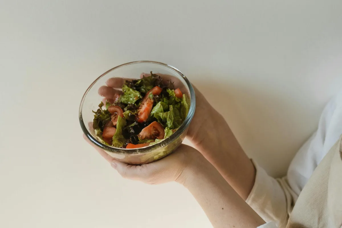 Nahaufnahme eines gesunden grünen Salats mit Tomaten in einer von Händen gehaltenen Glasschale