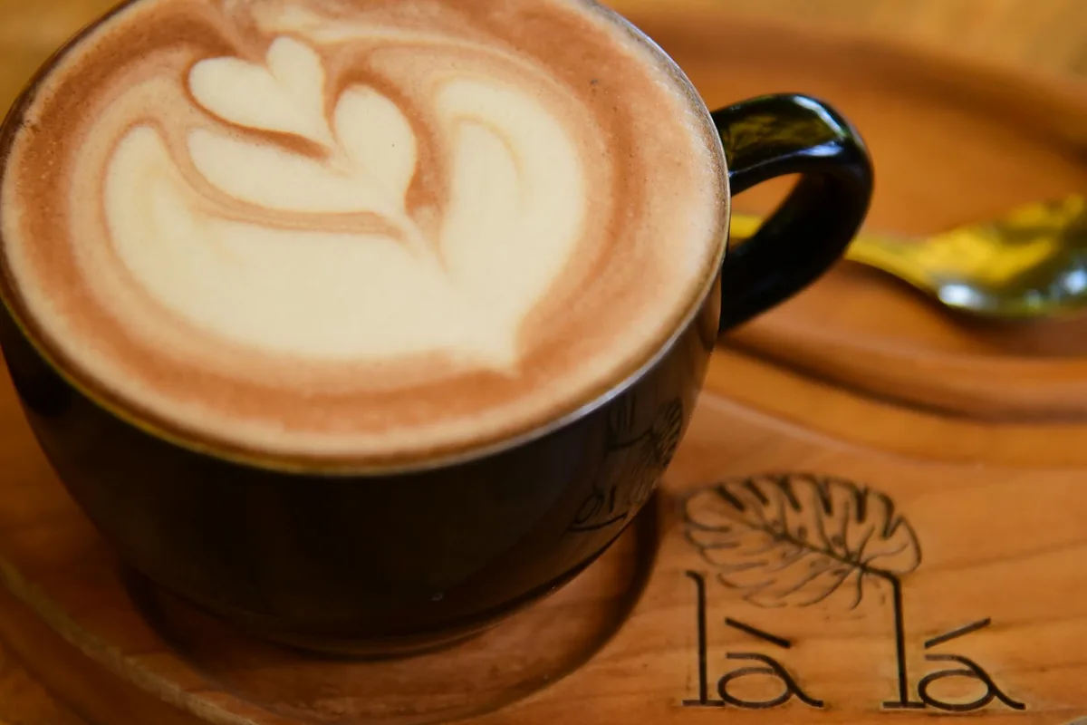 Close-up of a latte with heart-shaped art in a black mug on a wooden saucer.