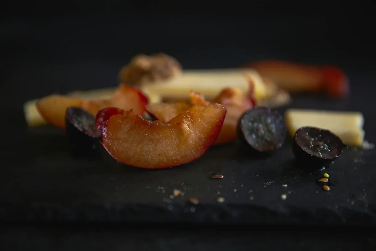 Nahaufnahme frischer Pflaumenscheiben auf schwarzem Schiefer mit Käse und Samen – Food-Blog-Visuals