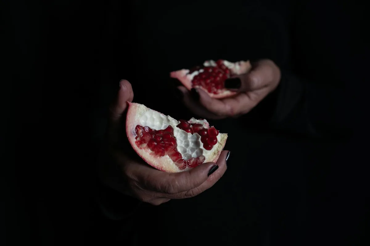 Nahaufnahme von Händen, die einen frischen Granatapfel in dunklem Licht halten