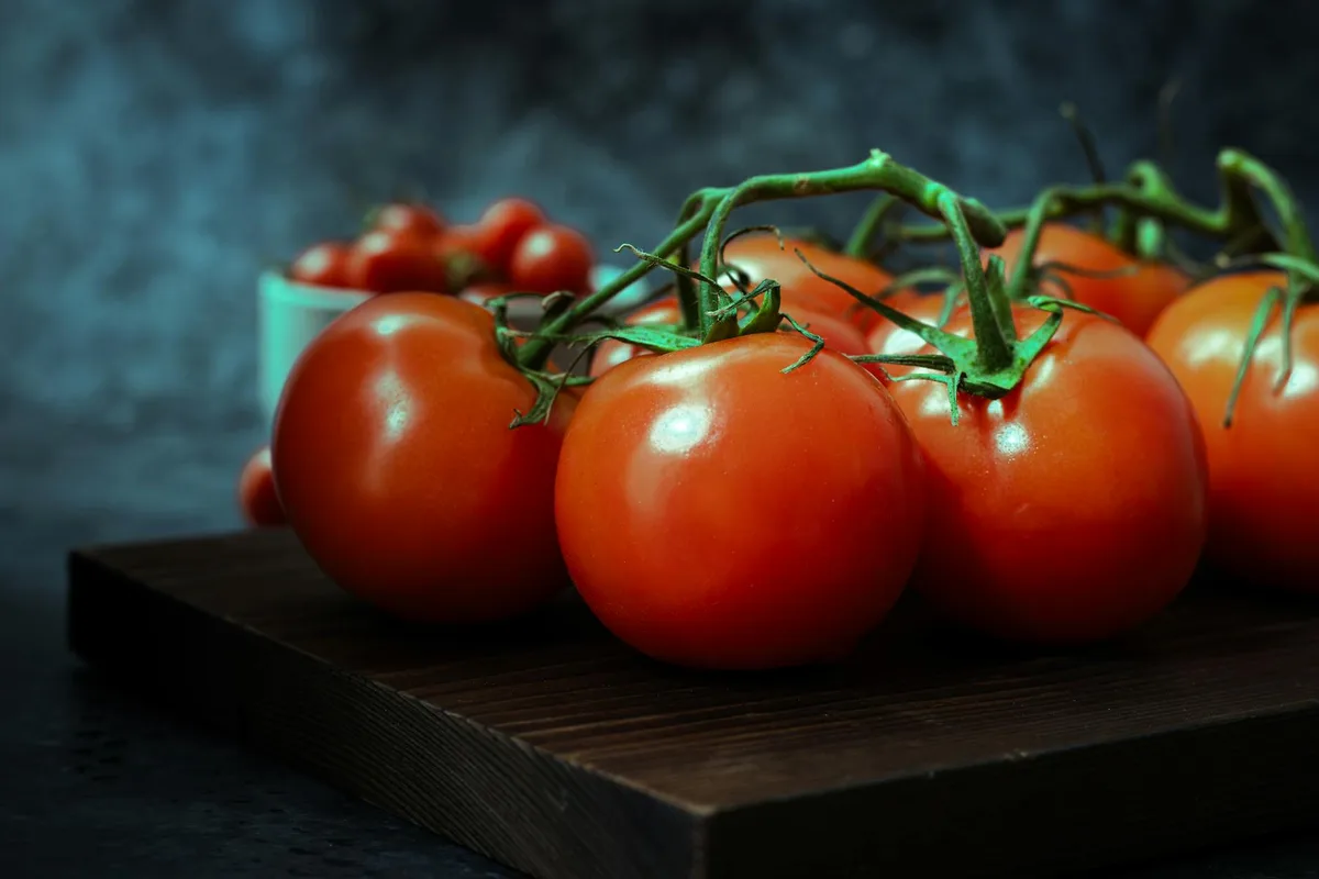 Tomates frescos con estética oscura en tabla de madera para fotografía gastronómica creativa