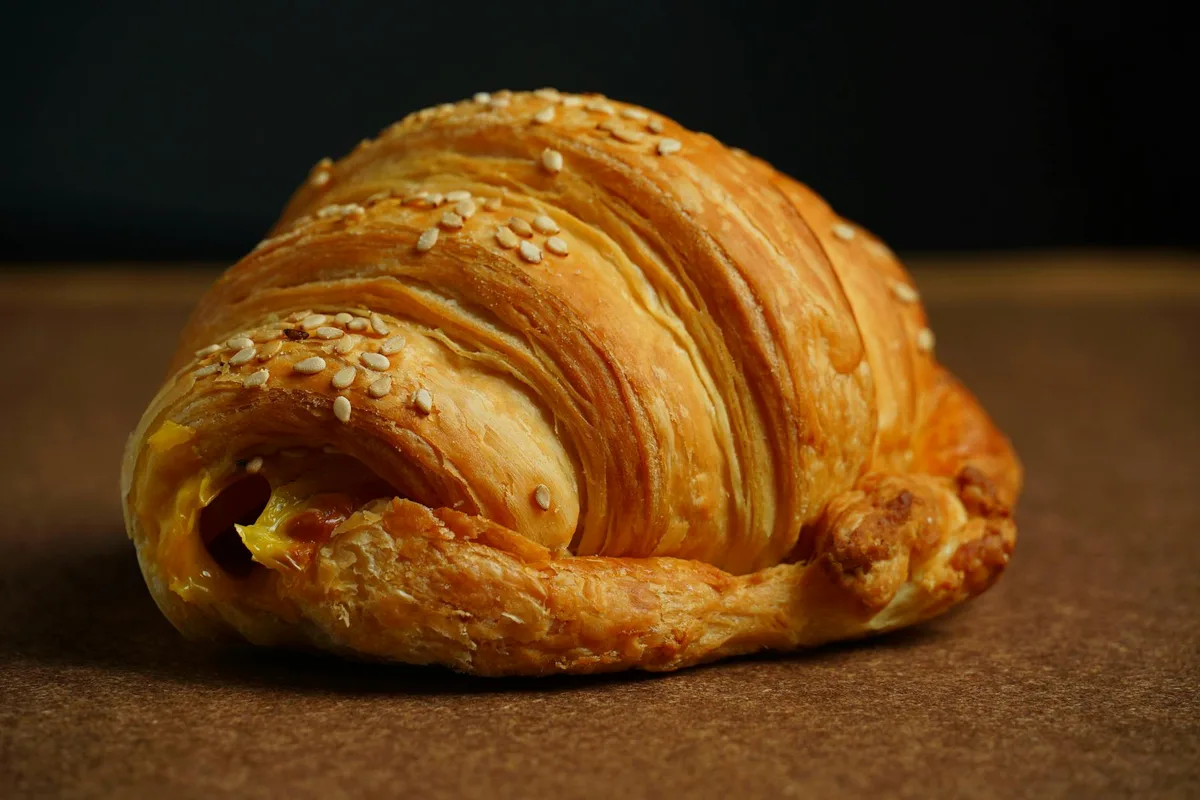 Croissant al formaggio dorato cosparso di semi di sesamo su superficie strutturata