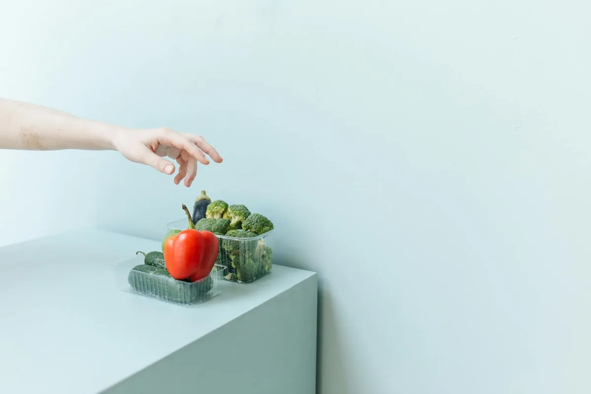 Hand greift nach frischem Gemüse auf minimalistischer weißer Oberfläche