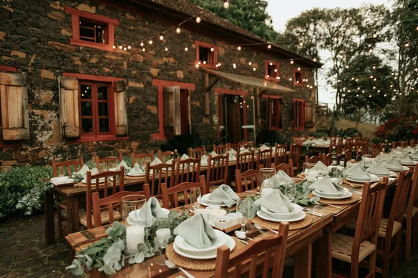 Outdoor rustic dinner setting with string lights, wooden tables, and stone building, creating a warm ambiance.