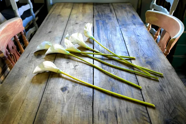 Rustic wooden table adorned with elegant calla lilies in a cozy dining room setting.
