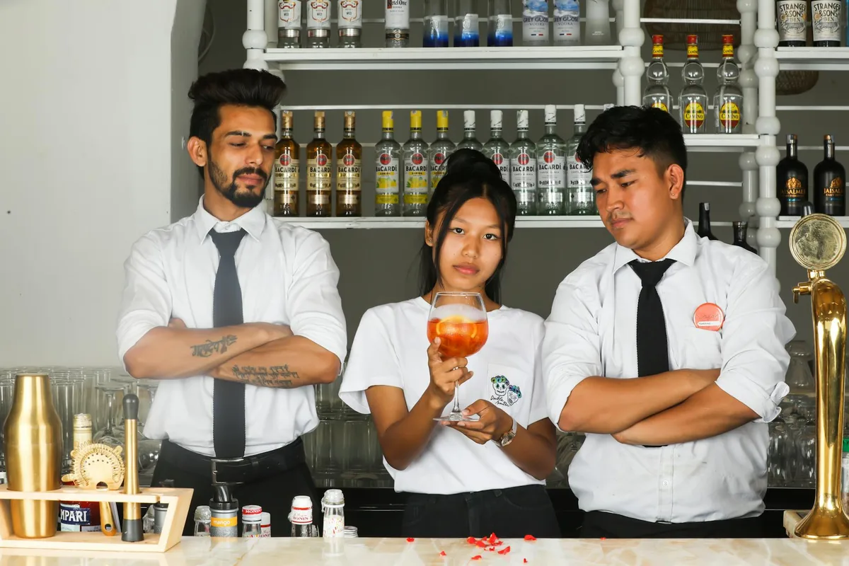 Tre baristi al bancone discutono di cocktail circondati da bottiglie di liquore