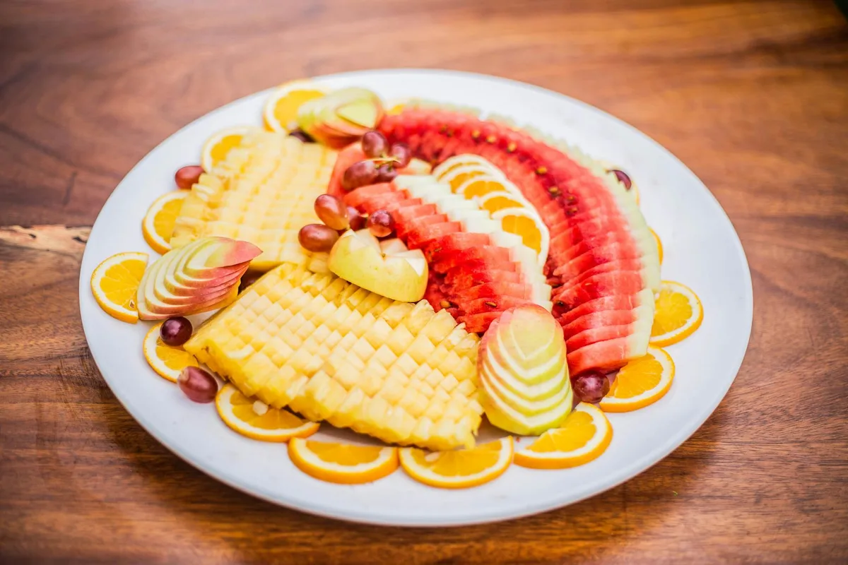 Vassoio di legno con anguria, arance, ananas, mele e uva fresche