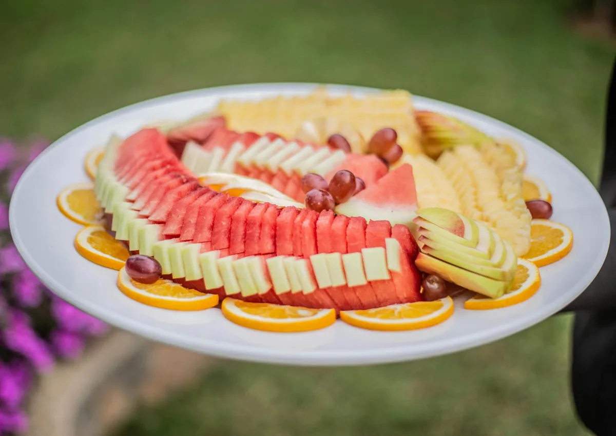 Macedonia di frutta vibrante con anguria, mela, arancia e uva su piatto bianco all'aperto