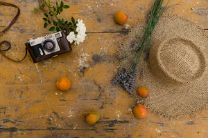 Vintage camera with rustic summer elements, apricots, and a straw hat on a wooden table.