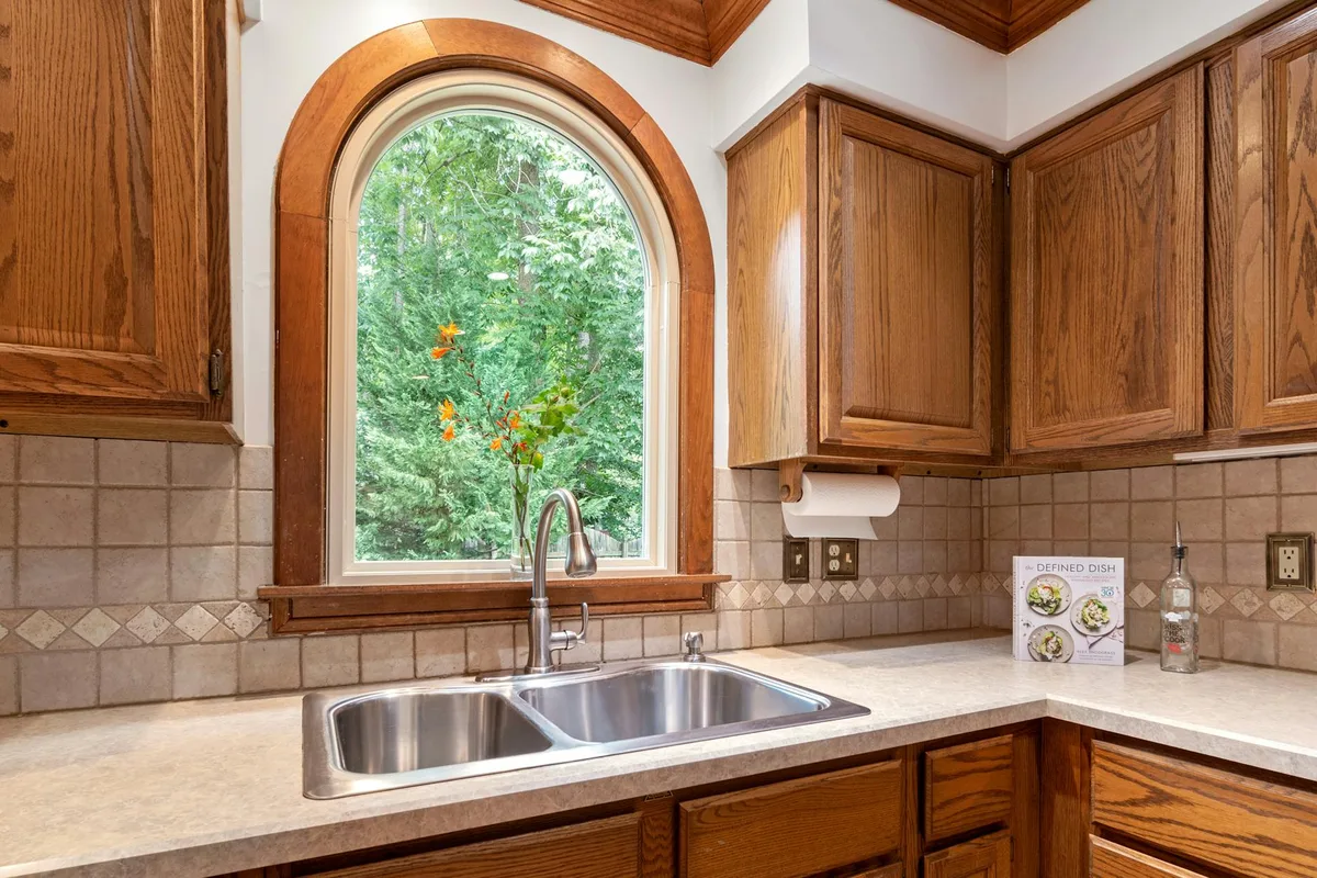 A traditional kitchen featuring wooden cabinets and a double sink with an arched window view.