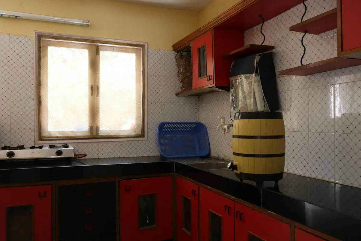 Cucina indiana luminosa con mobili rossi, fornello a gas e luce dalla finestra