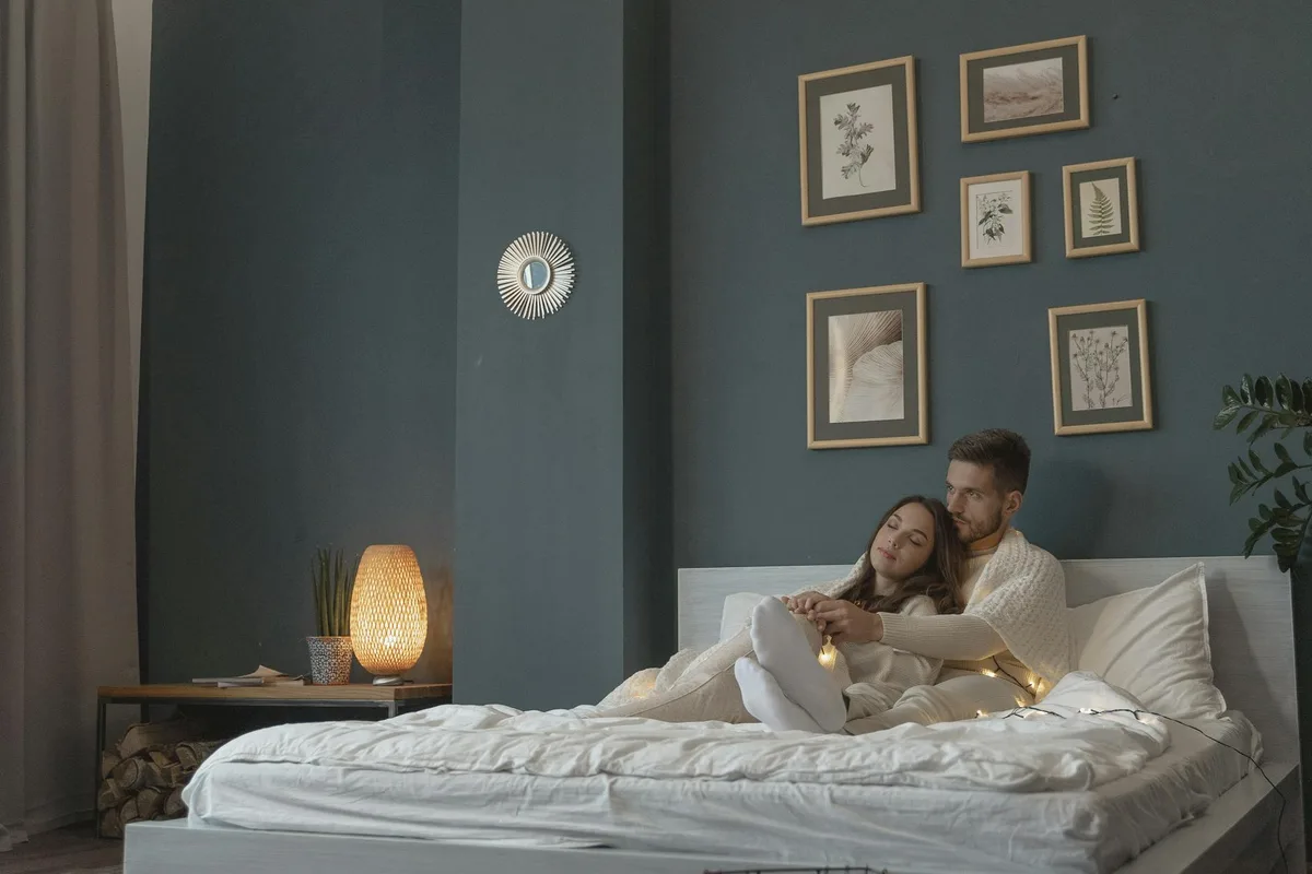 Casal relaxa em quarto moderno decorado com arte e luzes de fada, transmitindo aconchego