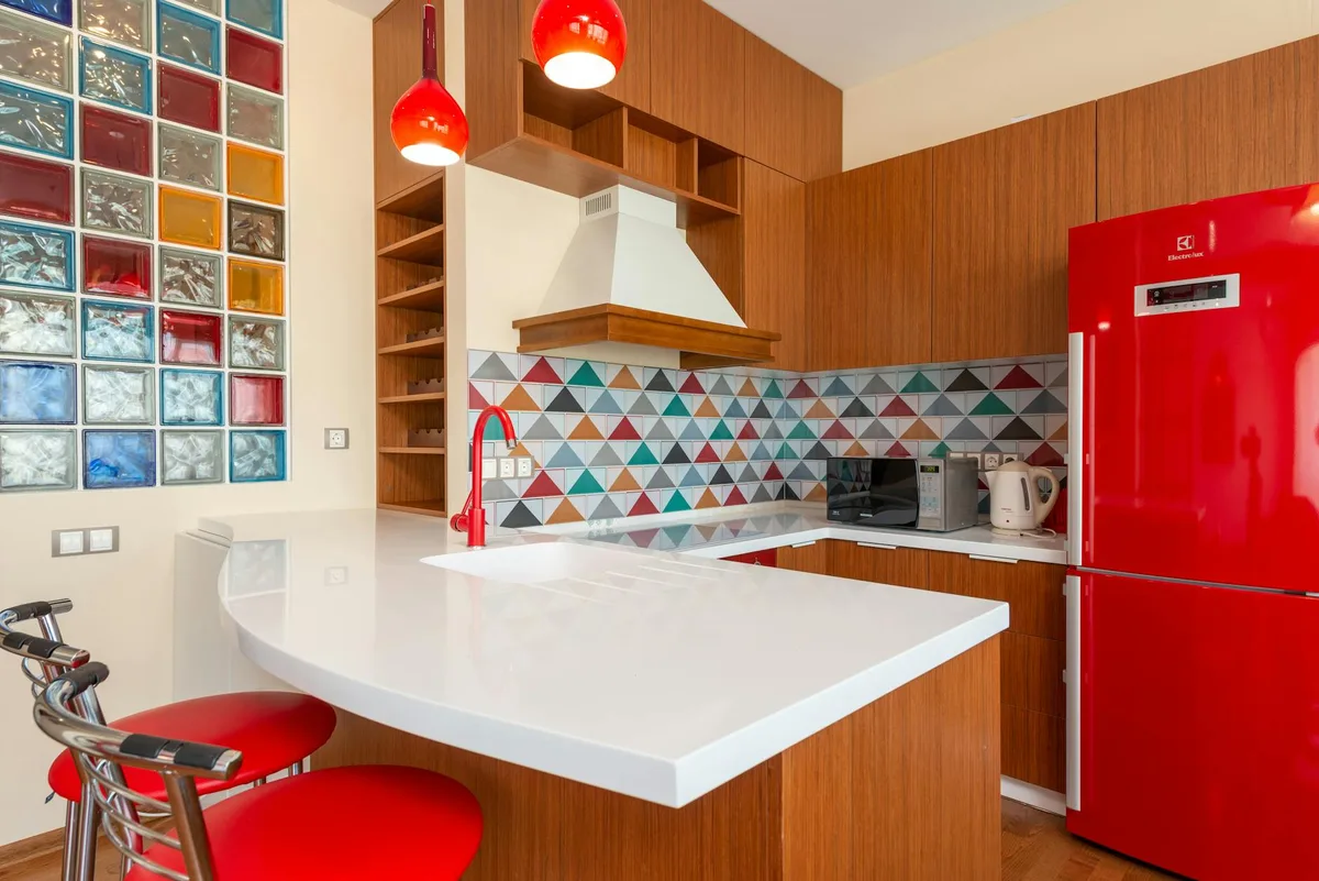 Interno di cucina moderna e vuota con frigorifero rosso e pareti colorate in appartamento di giorno