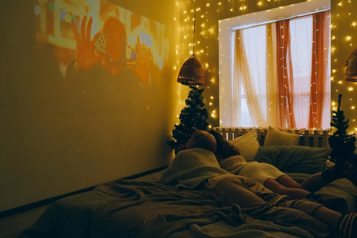 Pessoas assistindo filme em quarto decorado com luzes festivas e pequenas árvores de Natal