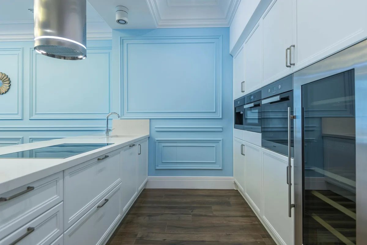 Moderne Küche mit weißen Schränken, blauer Akzentwand und Edelstahlgeräten