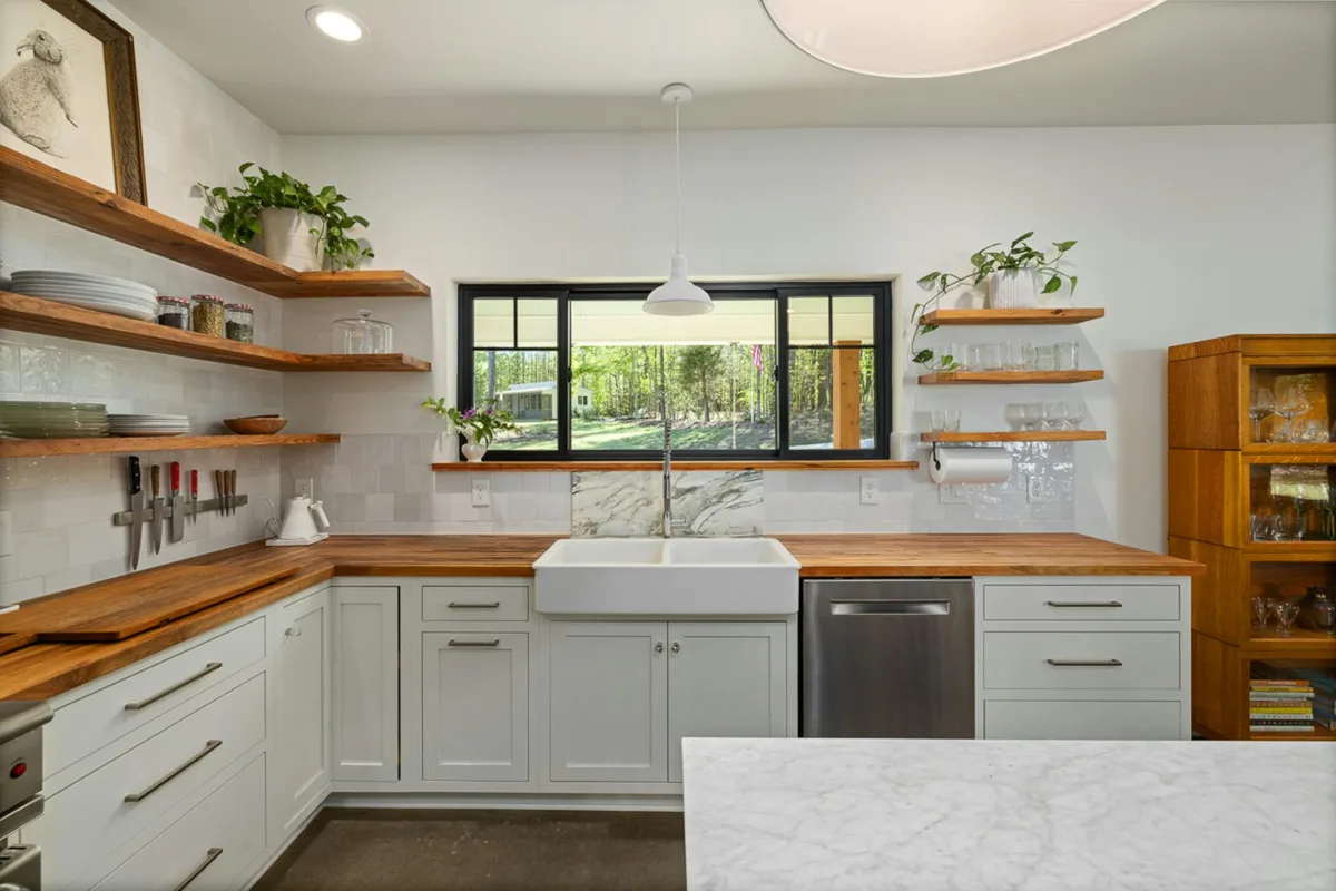 Stilvolle Küche mit offenen Regalen, Bauernspüle und Holzarbeitsplatten mit Ausblick nach draußen.