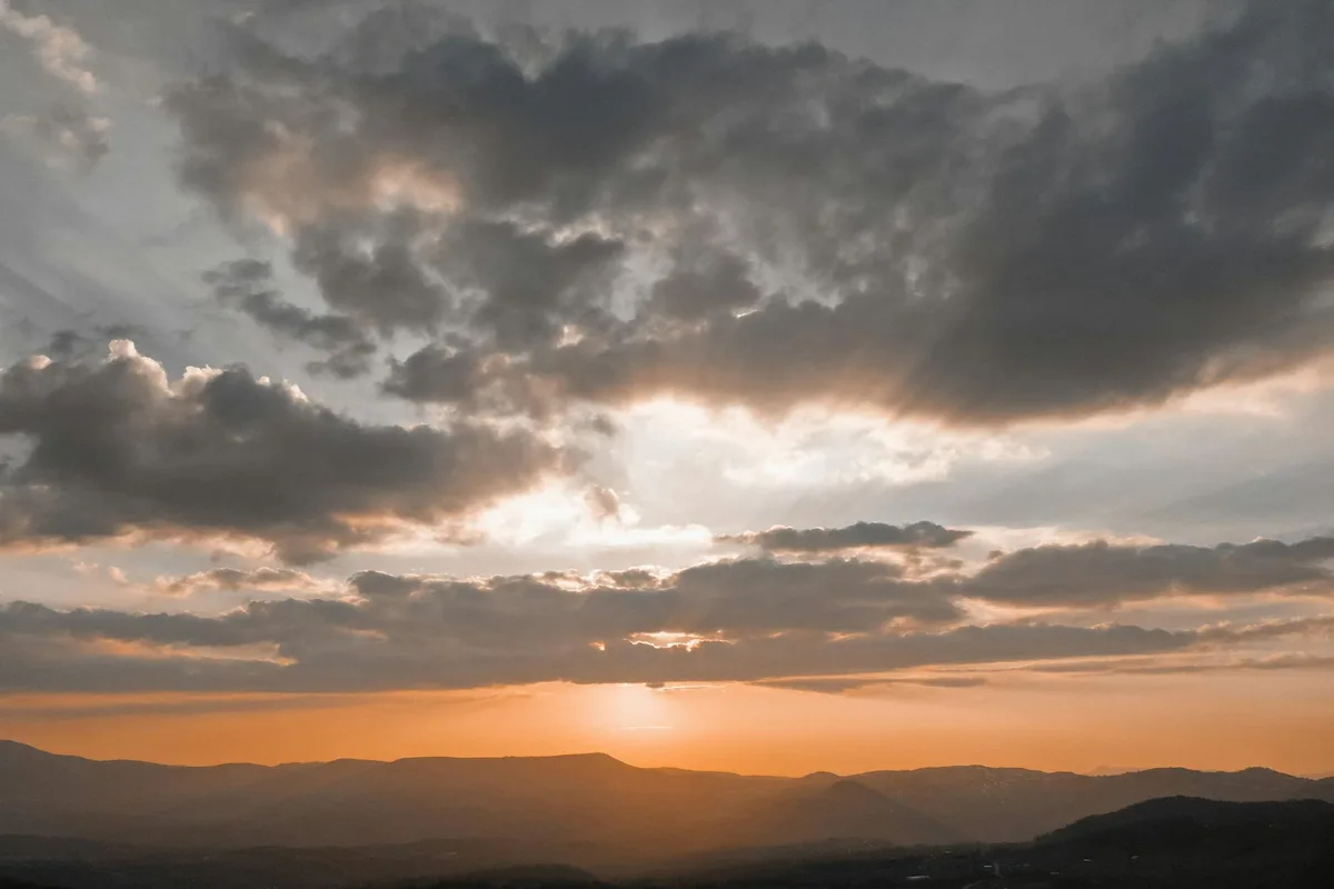 Atemberaubender Sonnenuntergang mit goldenen Farbtönen über einer bergigen Landschaft und dramatischen Wolken