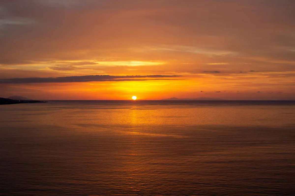 Vista mozzafiato di un tramonto arancione vibrante sull'orizzonte calmo dell'oceano.