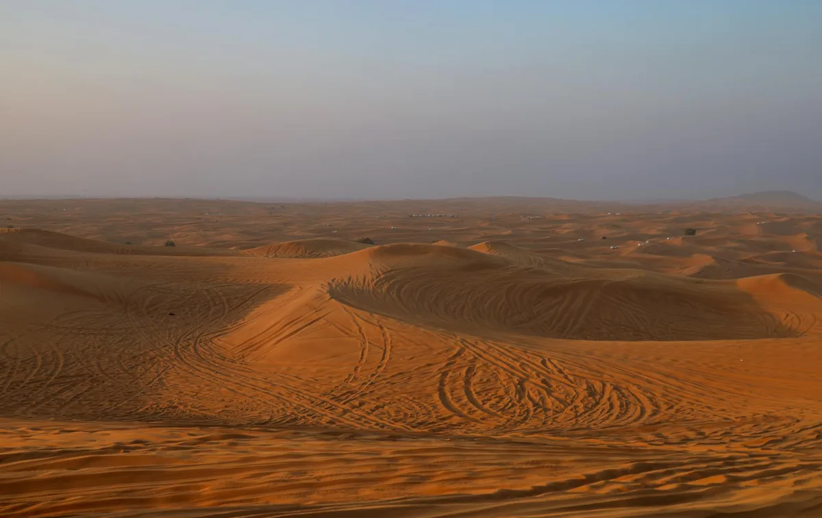 Vista mozzafiato di dune di sabbia sotto un cielo al tramonto, che cattura l'essenza della tranquillità desertica.
