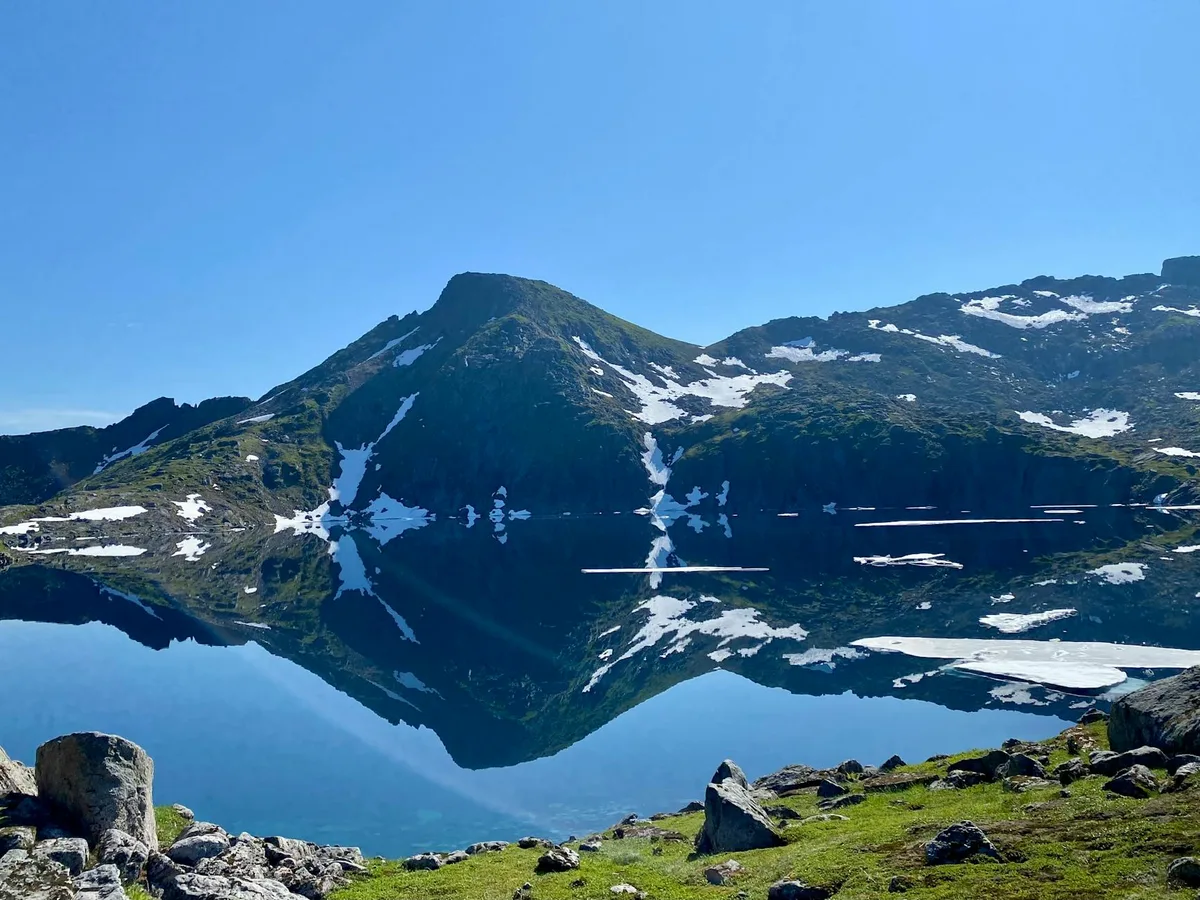 Lago di montagna cristallino che riflette vetta innevata sotto cielo azzurro brillante