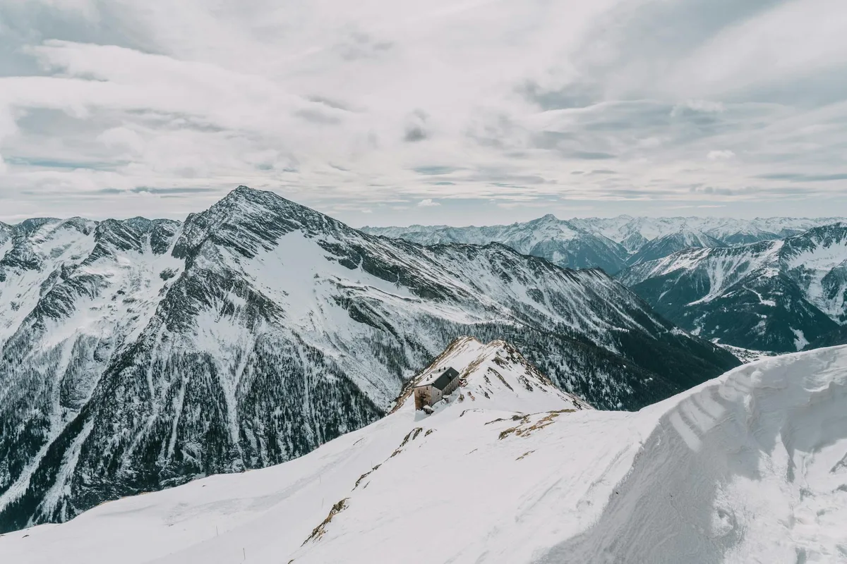 Scena invernale aspra con montagne innevate e baita isolata