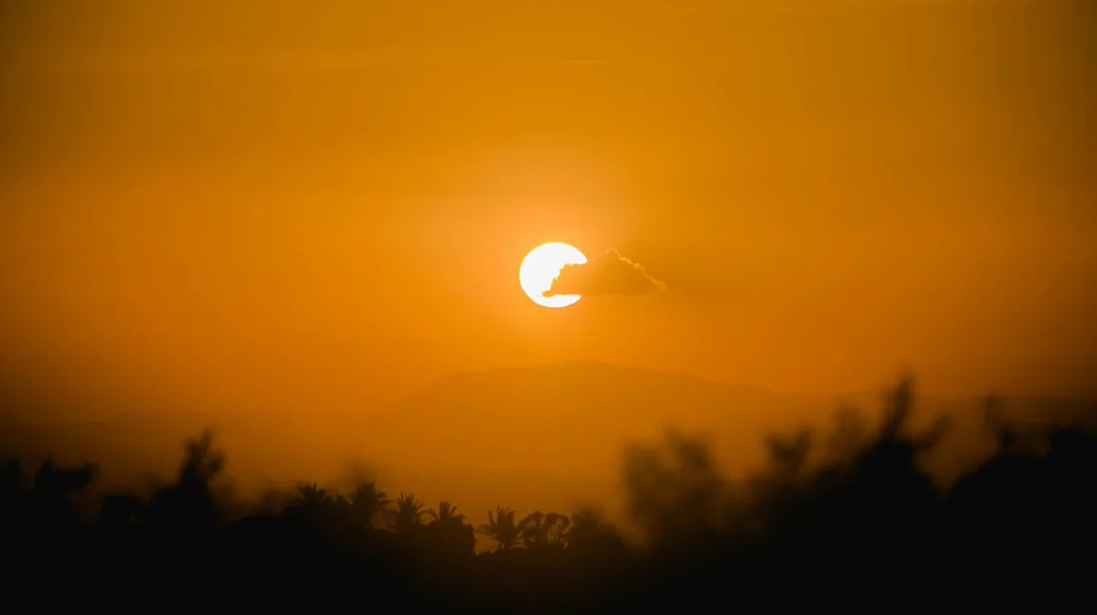 Goldener Sonnenuntergang mit einer Wolke, die Schatten auf silhouettierte Bäume und ferne Berge wirft