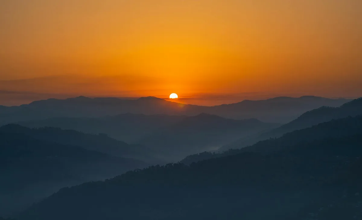 구릉과 산 위로 지는 노을이 연출한 따뜻하고 드라마틱한 하늘 풍경