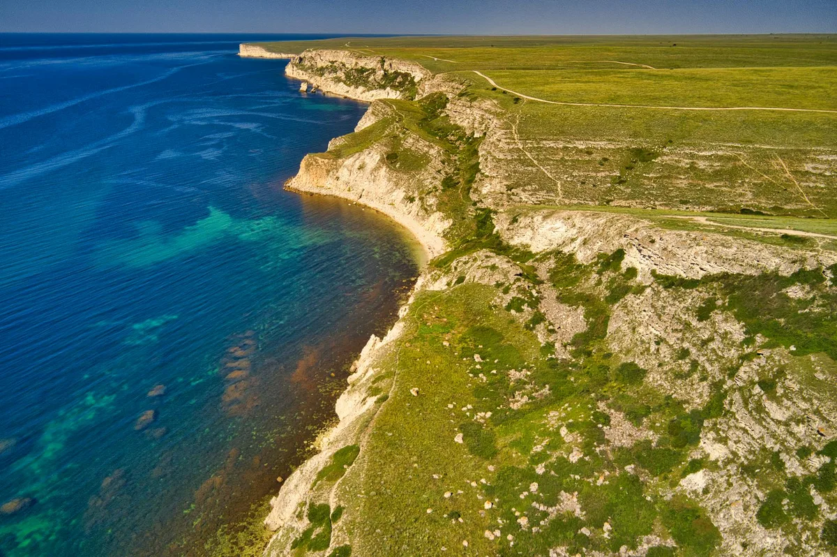 Ripresa aerea di una costa spettacolare con scogliere e acque azzurre, catturata dall'alto.
