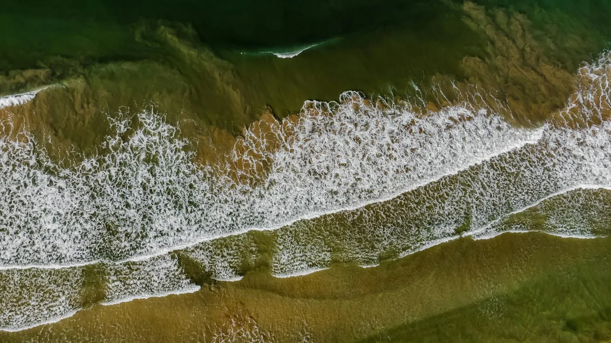 Ripresa aerea delle onde oceaniche che si infrangono sulla spiaggia di Bentota, Sri Lanka, mostrando pattern e bellezza naturali.