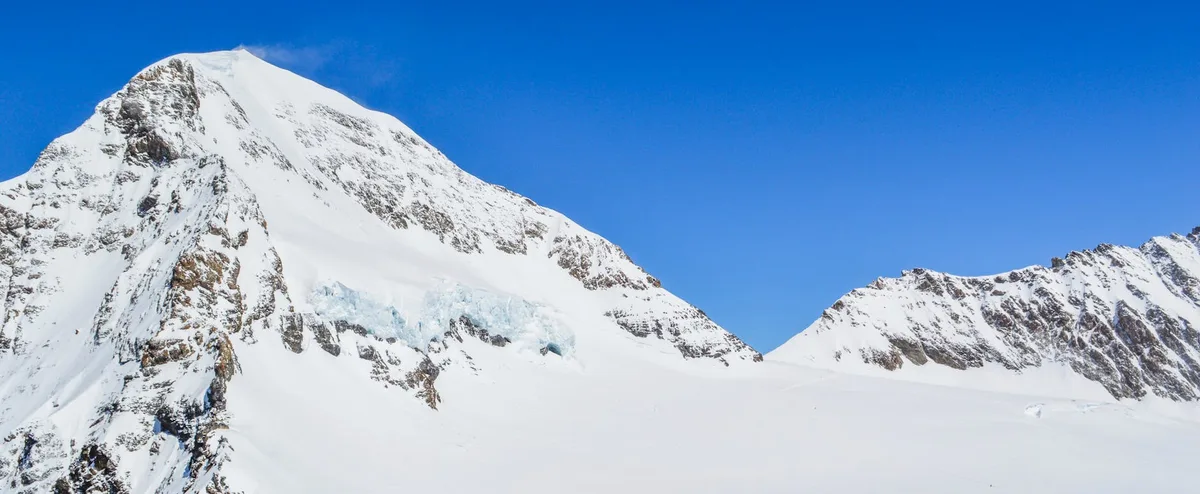 Paesaggio mozzafiato di aspri pendii montani innevati contro cielo azzurro