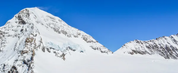 Paesaggio mozzafiato di aspri pendii montani innevati contro cielo azzurro