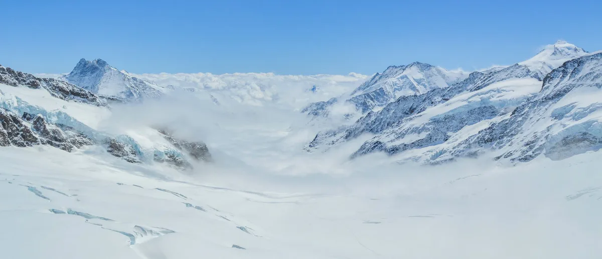 Panorama mozzafiato di vette montane con neve e nuvole su pendio contro cielo azzurro