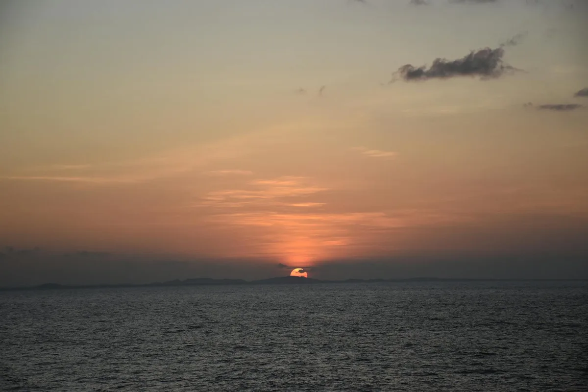 Tramonto vibrante su oceano calmo con silhouette di terra lontana