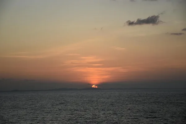 Tramonto vibrante su oceano calmo con silhouette di terra lontana