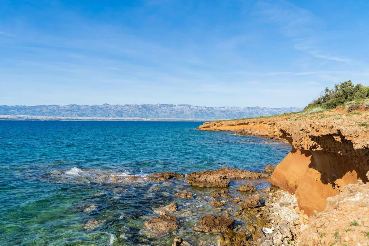 Costa croata con scogliere rocciose e acque azzurre sotto un cielo limpido
