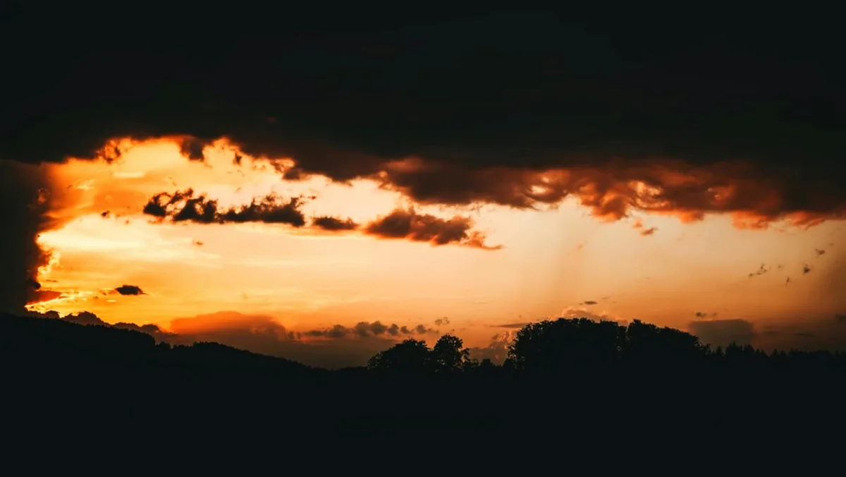 Orangefarbener Sonnenuntergang mit dramatischen dunklen Wolken und Baum-Silhouetten