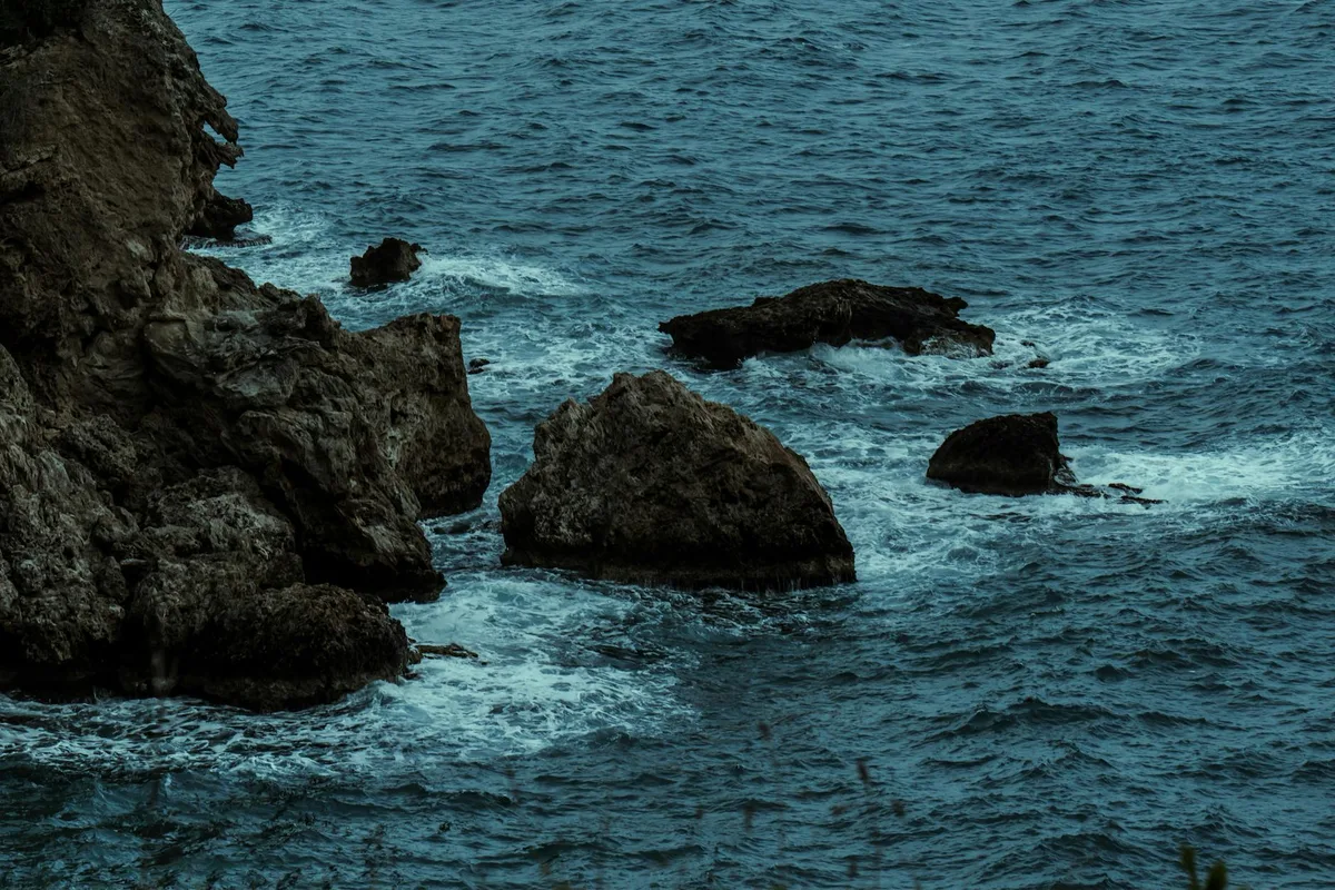 Costa rocciosa drammatica con onde del Mediterraneo al crepuscolo